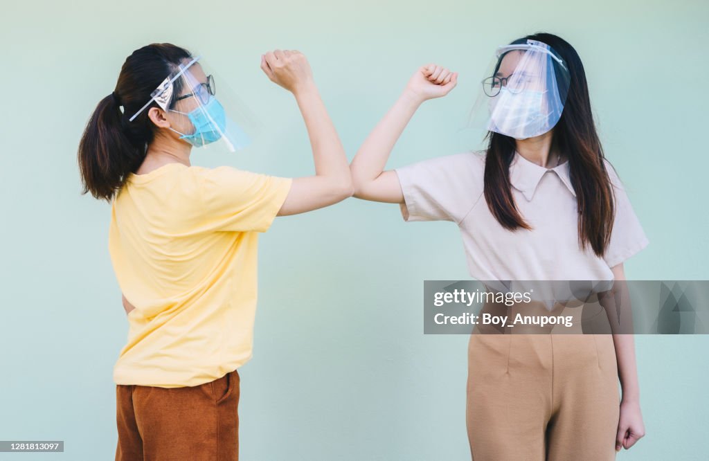 Two Asian women doing the elbows bump while greeting during covid-19 pandemic situation.