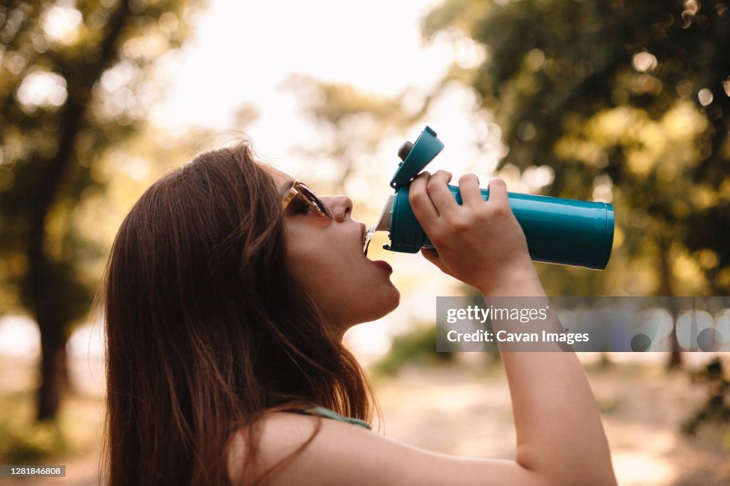 Young woman drinking water from reusable bottle in summer park