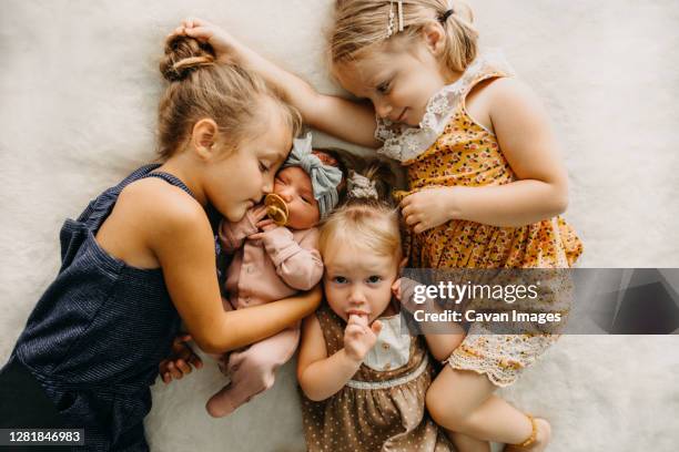 sisters cuddle in bed on white blanket with newborn baby - familie mit vier kindern stock-fotos und bilder