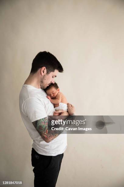 wide side view of tattooed millennial dad snuggling diapered newborn - baby father hug side stock-fotos und bilder