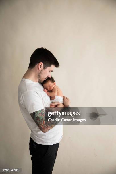 wide side view of tattooed millennial dad snuggling diapered newborn - baby father hug side stock pictures, royalty-free photos & images