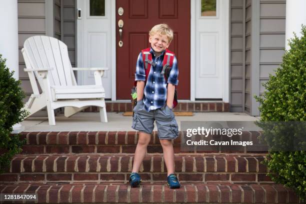 bashful, smiling, blonde boy stands on steps with hands in pockets - first day of summer imagens e fotografias de stock