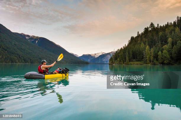 father paddling inflatable boat with son on lake. - baby boot stock-fotos und bilder