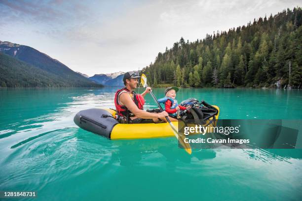 father and son laughing, enjoying paddling trip on turquoise lake. - baby boot stock-fotos und bilder