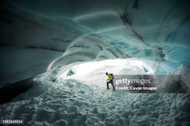 backpacker explores the inside a glacial ice cave. - winter adventure stock pictures, royalty-free photos & images