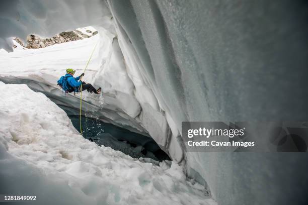 mountaineer rappels into glacier cave. - potholing stock pictures, royalty-free photos & images