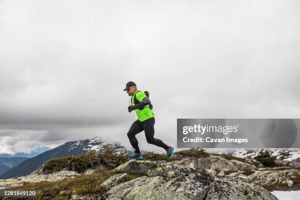 side view of fit active man trail running on mountain ridge. - ultramarathon stock-fotos und bilder