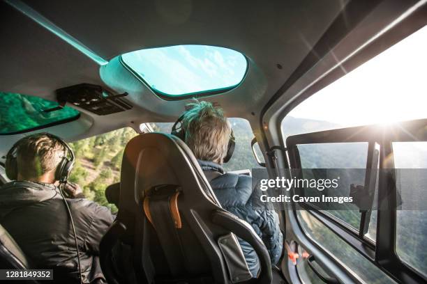 rear view of helicopter pilot flying low through forested mountains. - inside helicopter stock pictures, royalty-free photos & images