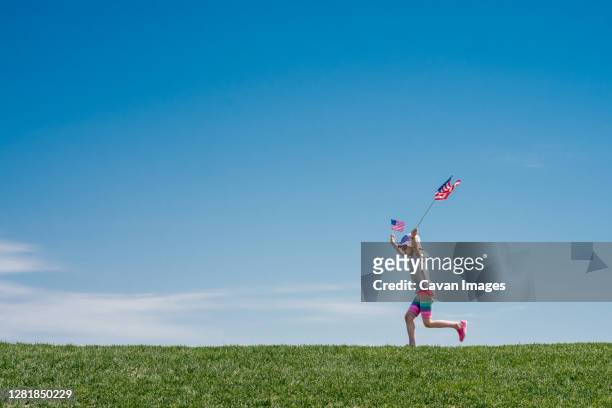young girl leaps across a grass hill waving 2 american flags - denver summer stock pictures, royalty-free photos & images