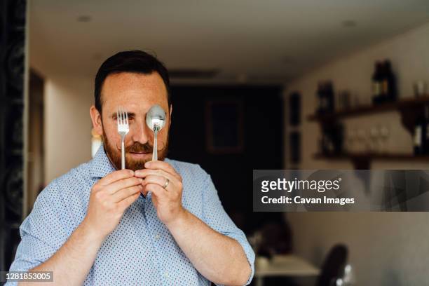 man with moustache holding fork and spoon in front of his face - spoon in hand stock-fotos und bilder