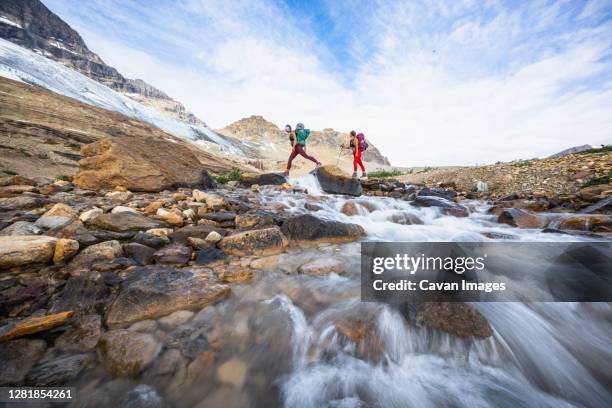 female backpackers crossing river while hiking beautiful iceline trail - yoho national park stock pictures, royalty-free photos & images