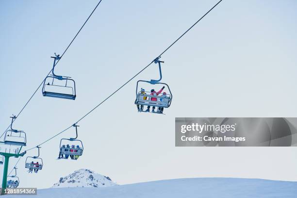 skiers on a chairlift looking down with a blue background - ski lift stock pictures, royalty-free photos & images