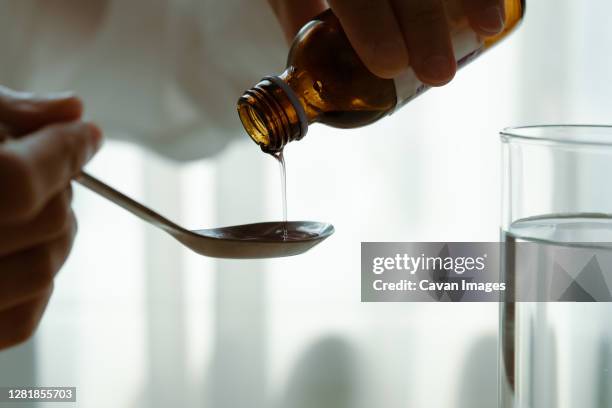 woman hand pouring medication or cough syrup from bottle to spoo - syrup stockfoto's en -beelden