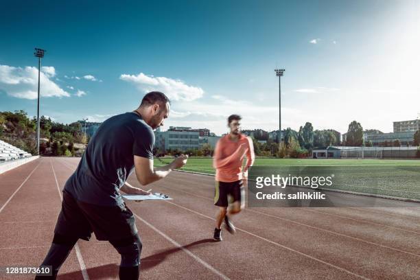 runner and coach doing sports training on track and field. the coach is measuring results with a stopwatch - coach stock pictures, royalty-free photos & images