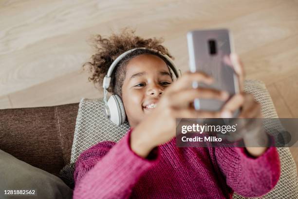 cute little african american girl is using mobile phone at home - lying on back girl on the sofa stock pictures, royalty-free photos & images