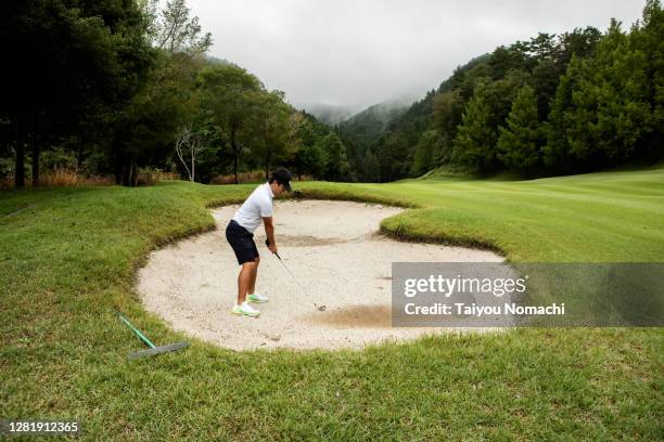 a man aims at the green from a bunker - golf bunker stock-fotos und bilder