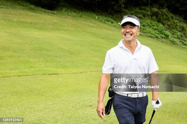 japanese man walking down the fairway with a smile - male golfer stock pictures, royalty-free photos & images