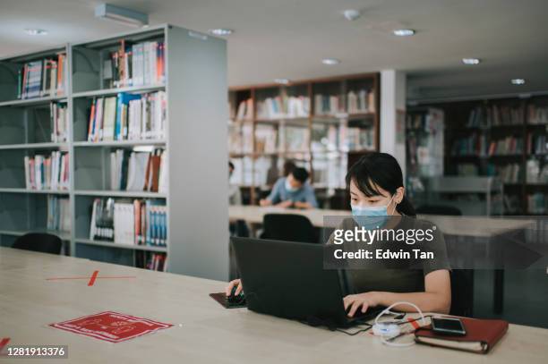 asian university student studying in library observing social distancing - university covid stock pictures, royalty-free photos & images