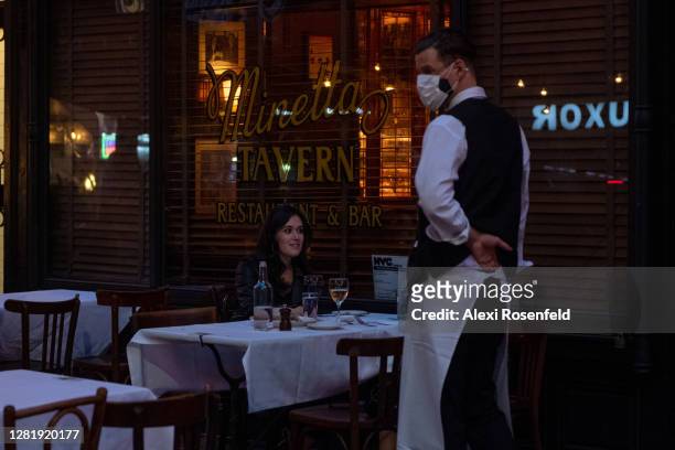 Waiter wearing a mask stands near customers eating outdoors at Minetta Tavern on October 23, 2020 in New York City. The pandemic continues to burden...