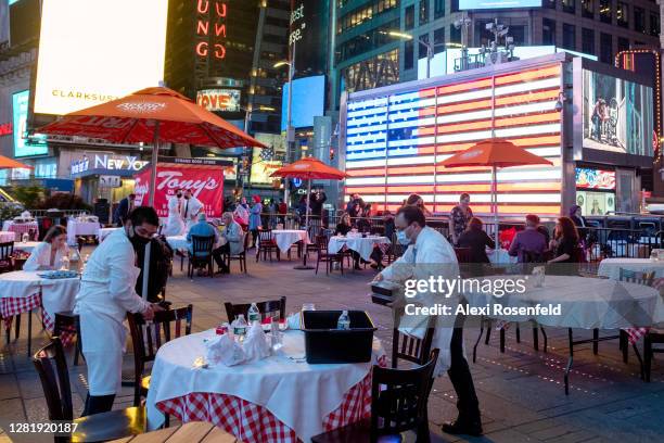 Waiters wearing masks clear a table at Tony's Di Napoli outdoor seating during the Taste of Times Square restaurant week near an American Flag on...