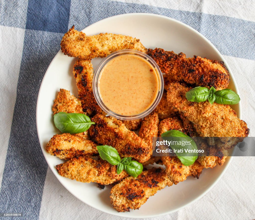 Chicken fingers in bowl with sauce over white kitchen towel.