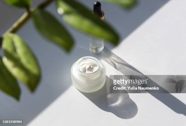 cosmetic cream and serum, flower leaves. natural hard light, deep shadows. - cosmetics cream stock pictures, royalty-free photos & images