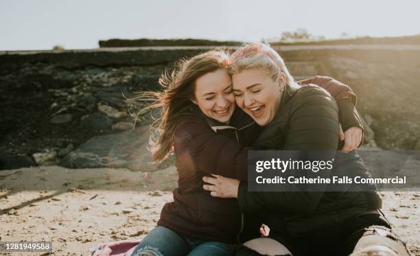 two laughing female hug each other tightly on the beach - good news stock pictures, royalty-free photos & images