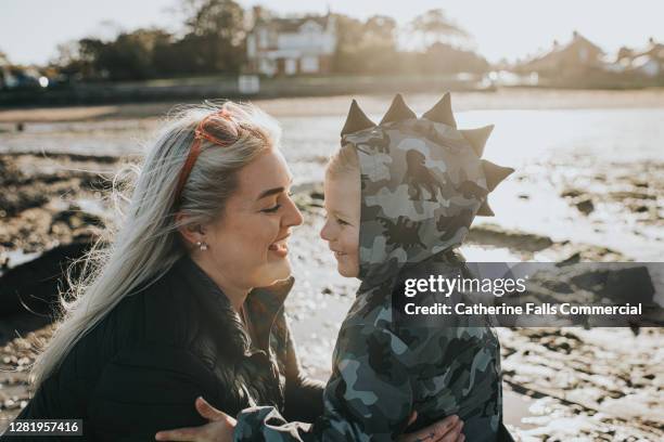 loving mother looks adoringly at her son on a cold sunny beach - mothers day beach fotografías e imágenes de stock