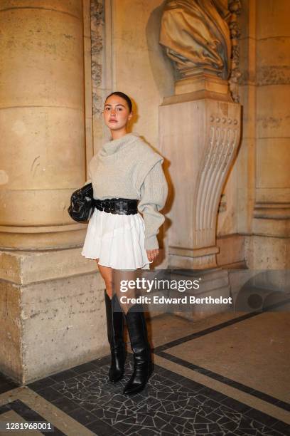 Sophia Roe wears a beige wool oversized pullover, a black leather large belt, a white short pleated skirt, a black leather Bottega Veneta bag, black...