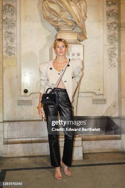 Camille Charriere wears a large jacket with puff sleeves, a beige top, black leather pants, a Chanel bag, a golden bracelet, outside Isabel Marant,...