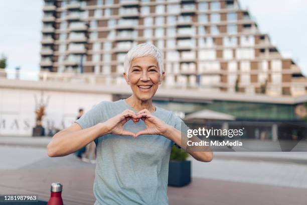 porträt einer aktiven seniorin, die ein herz zeigt - coole oma stock-fotos und bilder