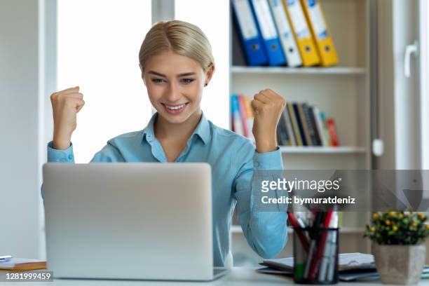 hhappy young woman celebrating at her desk in a office - bid offer stock pictures, royalty-free photos & images