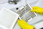 Person in a protective rubber glove washes in the sink air filter of the ventilation return duct blocked by dust and debris. Cleaning service.