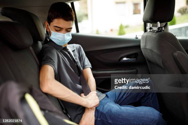teenage boy with face protective mask fastening seatbelt in the car - belt stock pictures, royalty-free photos & images
