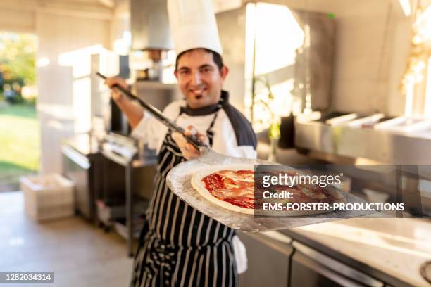 pizzaiolo at work - chef is shovelling the pizza in the burning oven. - pizzeria - fotografias e filmes do acervo