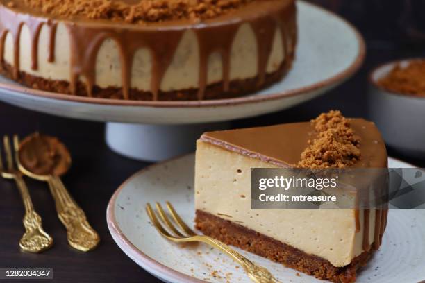 nahaufnahme von toffee karamell-käsekuchen-scheibe, butter-keks-basis, flauschige mascarpone frischkäse-topping mit toffee-karamell-sauce bedeckt, verziert mit kekskrümeln, braun umrandet weiße teller, marmor hintergrund, fokus auf den vordergrund - karamell stock-fotos und bilder