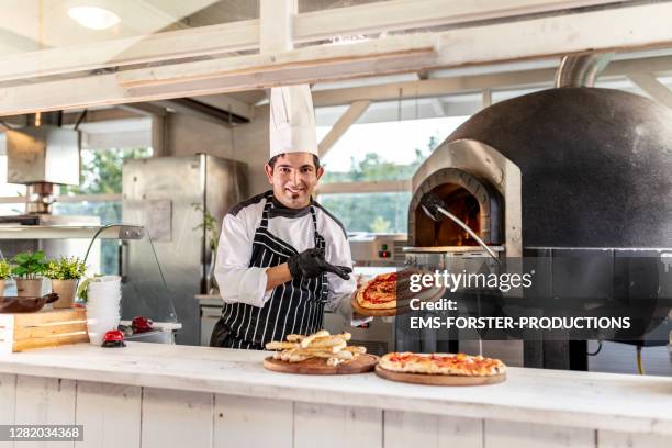 pizzaiolo at work - chef is showing fresh baked pizza in outdoor kitchen - pizzeria foto e immagini stock