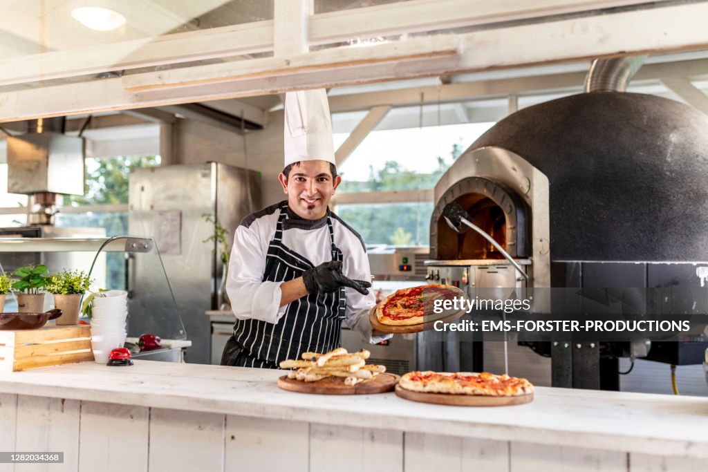 PIZZAIOLO AT WORK - chef is showing fresh baked pizza in outdoor kitchen