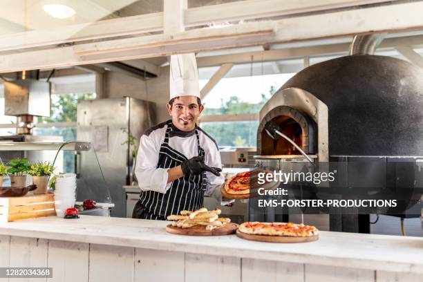 pizzaiolo at work - chef is showing fresh baked pizza in outdoor kitchen - pizzeria stockfoto's en -beelden