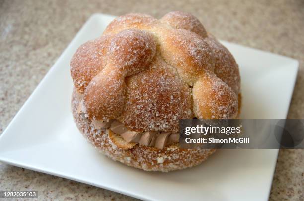 pan de muerto, filled with chocolate cream, on a white plate on a stone kitchen benchtop - pan de muerto stockfoto's en -beelden