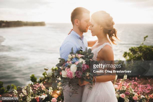 sunset wedding ceremony outdoors in bali. young couple kissing in love - hochzeitspaar stock-fotos und bilder
