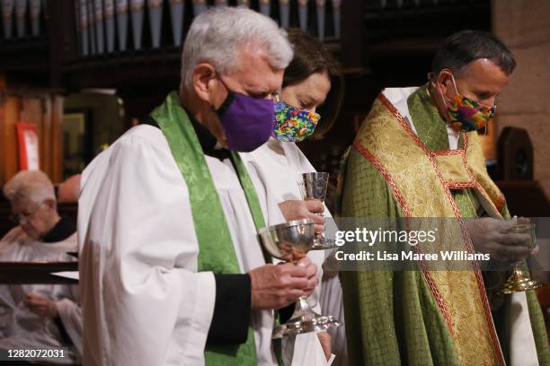 Father Michael Deasey, Lay Minister Rosemary King and Father James Collins wear face masks as they prepare to distribute the holy communion during...