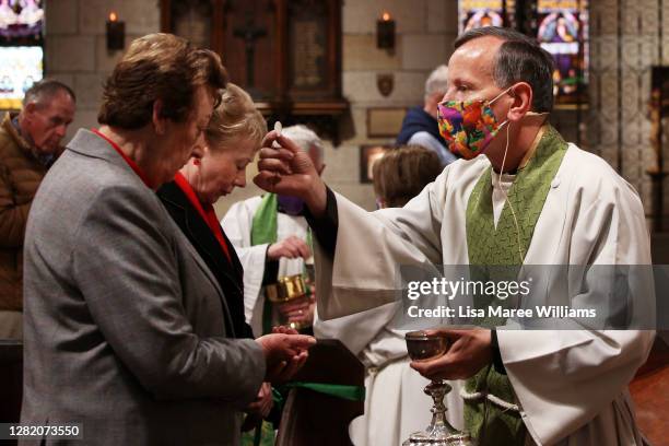 Father James Collins wears a face mask as he distributes the holy communion during the 'Twenty-First Sunday after Pentecost' service at St Paul's...