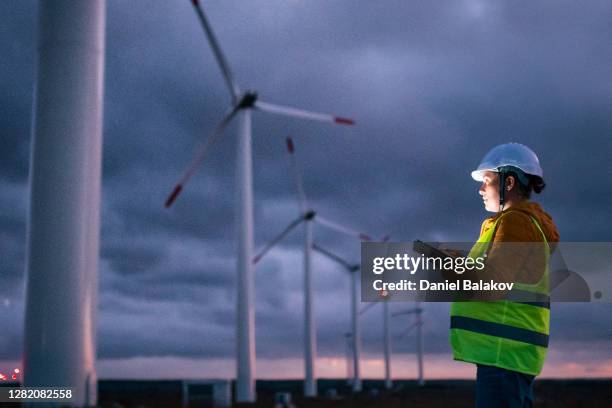 erneuerbare energiesysteme. strom-wartungsingenieur arbeitet auf dem feld in einem windturbinenkraftwerk in der dämmerung mit einem launischen himmel dahinter. verschwommene bewegung. - impacto stock-fotos und bilder