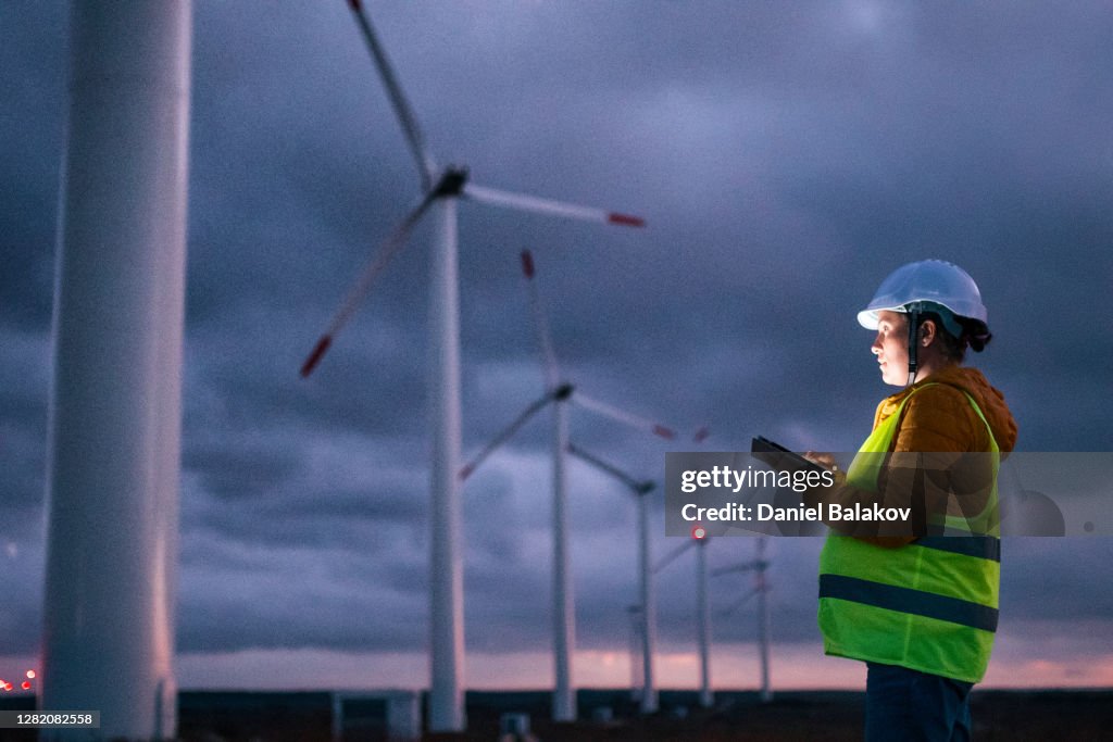Sistemas de Energia Renovável. Engenheiro de Manutenção de Eletricidade trabalhando no campo em uma estação de energia de turbina eólica ao anoitecer com um céu mal-humorado atrás. Movimento borrado.