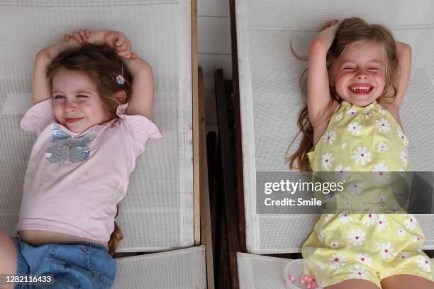 two happy young girls relaxing on deck chairs - 2 peas in a pod stock pictures, royalty-free photos & images