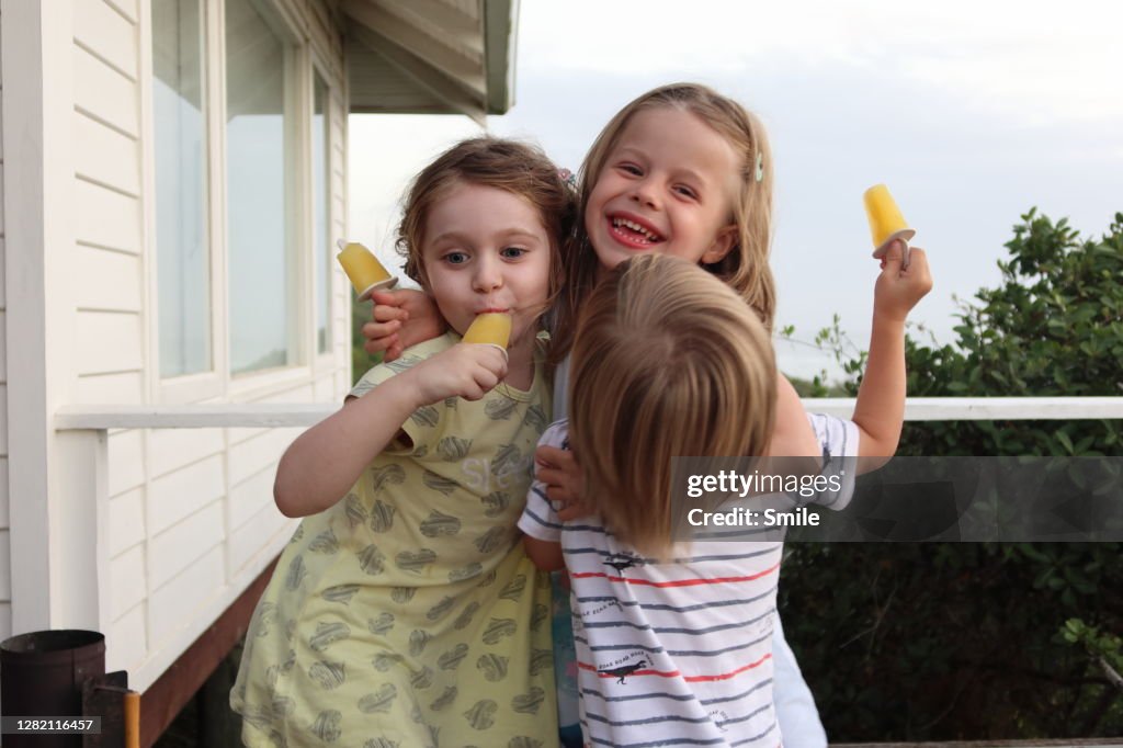 Three delighted young children embracing with ice lollies