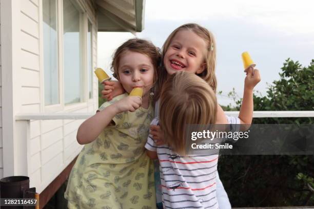 three delighted young children embracing with ice lollies - 2 peas in a pod stock pictures, royalty-free photos & images