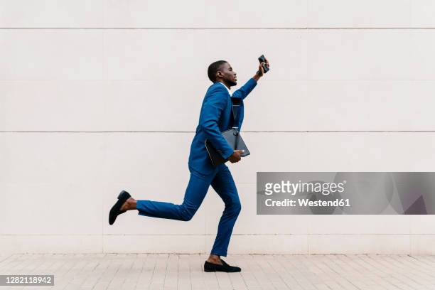 young male professional running on sidewalk by wall in city - african map stockfoto's en -beelden