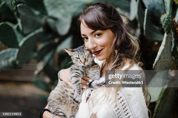 young woman smiling while holding cat against plant - cat hipster no stock pictures, royalty-free photos & images